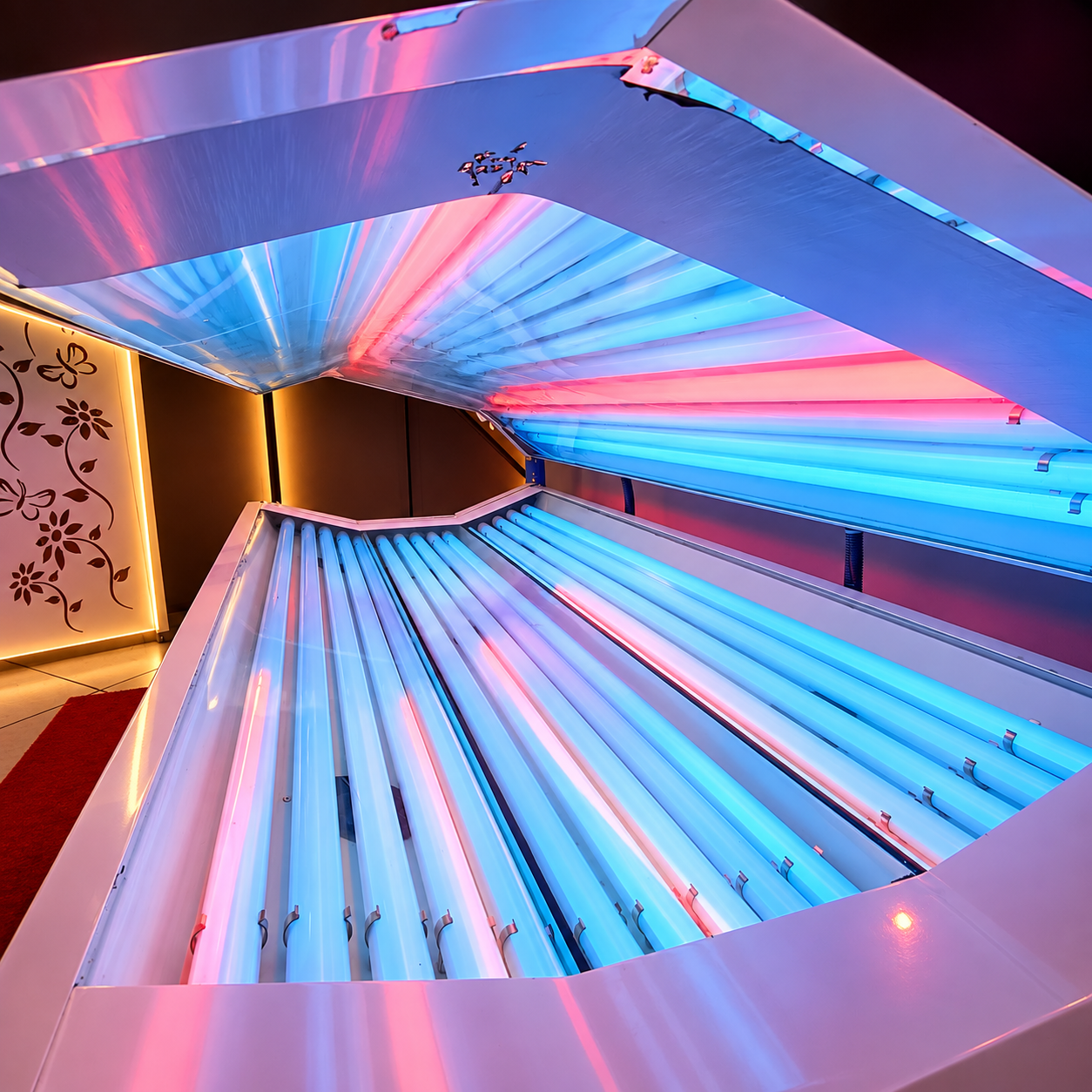 Máquina deitada de bronzeamento aberta, com lâmpadas acesas em tons azul e rosa